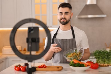 Photo of Food blogger cooking while recording video with smartphone and ring lamp in kitchen