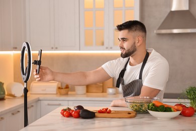 Photo of Food blogger cooking while recording video with smartphone and ring lamp in kitchen