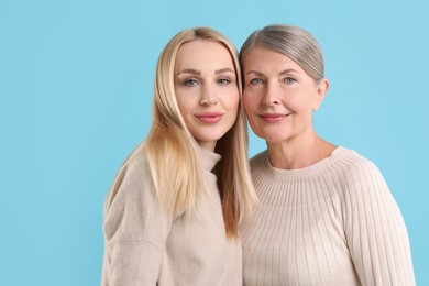 Family portrait of young woman and her mother on light blue background