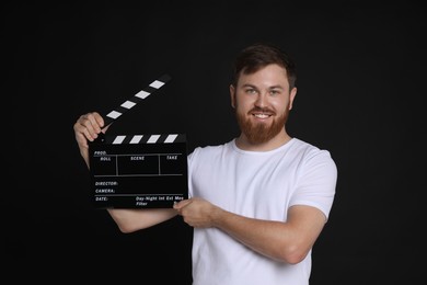 Photo of Making movie. Happy man with clapperboard on black background