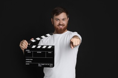 Photo of Making movie. Happy man with clapperboard pointing at camera on black background