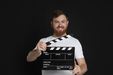 Making movie. Happy man with clapperboard on black background