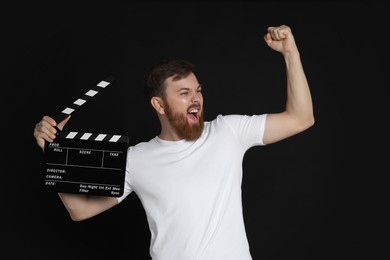 Photo of Making movie. Happy man with clapperboard on black background