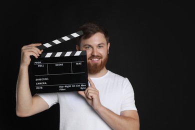 Making movie. Smiling man with clapperboard on black background. Space for text