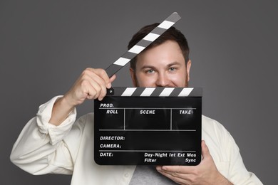 Making movie. Man with clapperboard on grey background