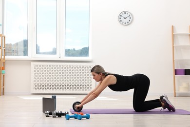 Online fitness trainer. Woman doing exercise with ab roller near laptop at home