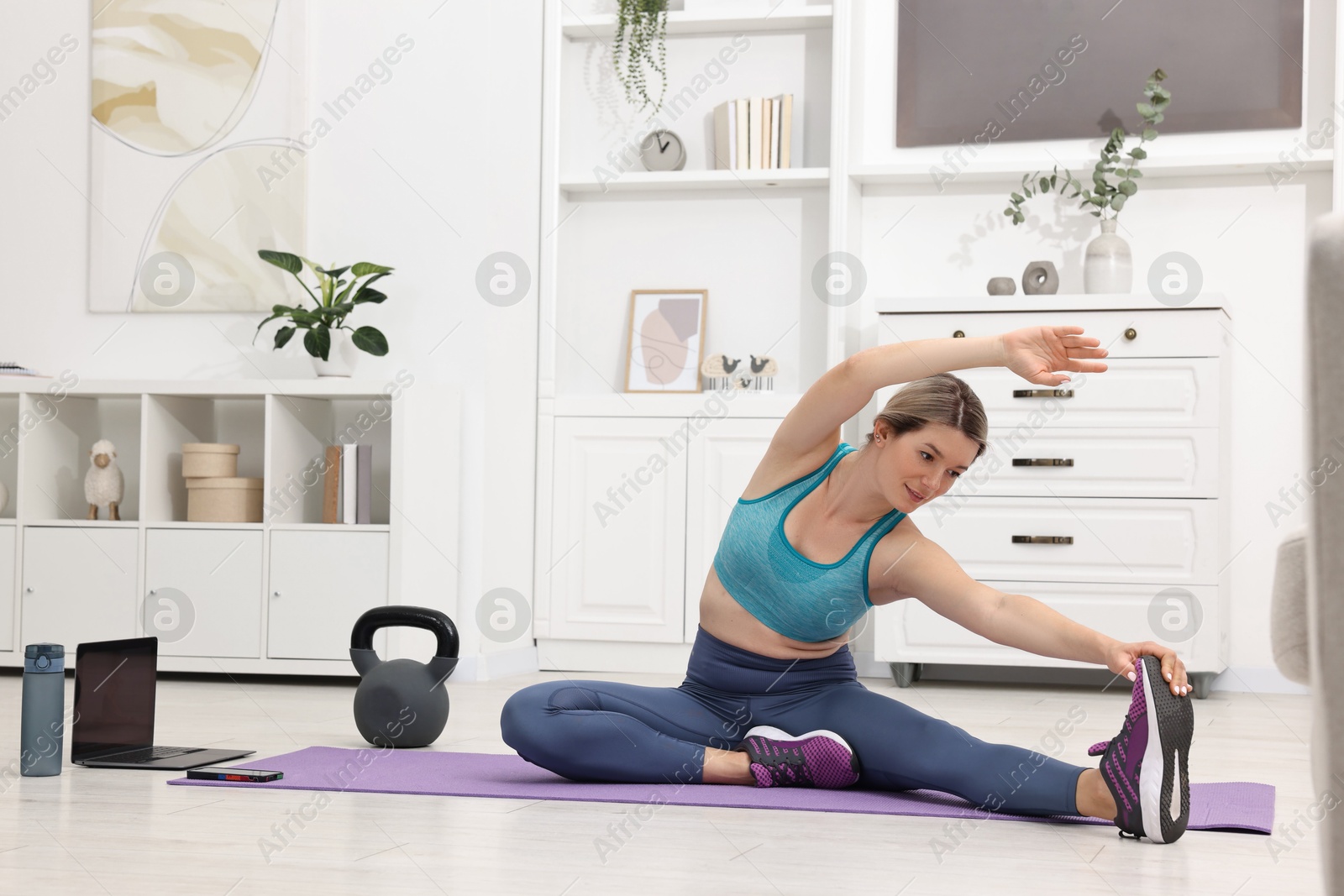 Photo of Online fitness trainer. Woman doing exercise near laptop at home