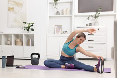 Online fitness trainer. Woman doing exercise near laptop at home