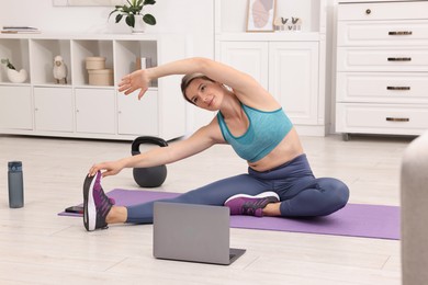 Online fitness trainer. Woman doing exercise near laptop at home