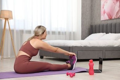 Photo of Online fitness trainer. Woman stretching near laptop at home