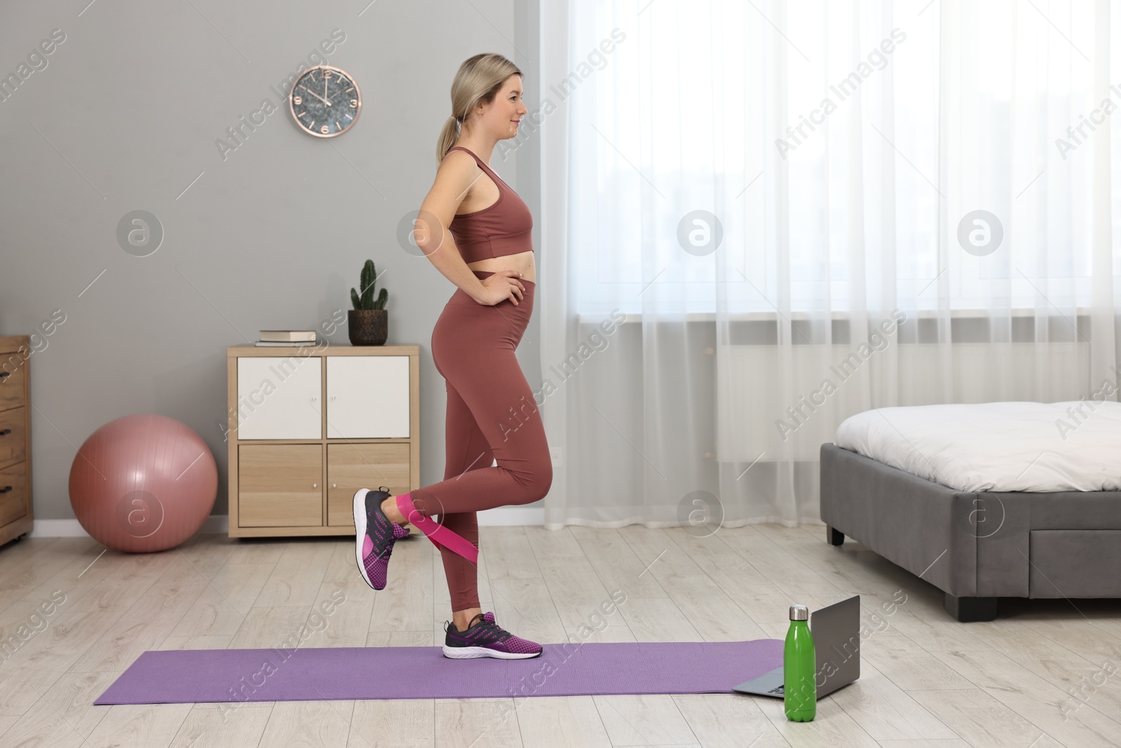 Photo of Online fitness trainer. Woman doing exercise with elastic band near laptop at home