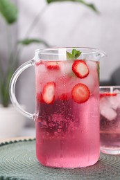 Photo of Freshly made strawberry lemonade with mint in jug and glass on table indoors