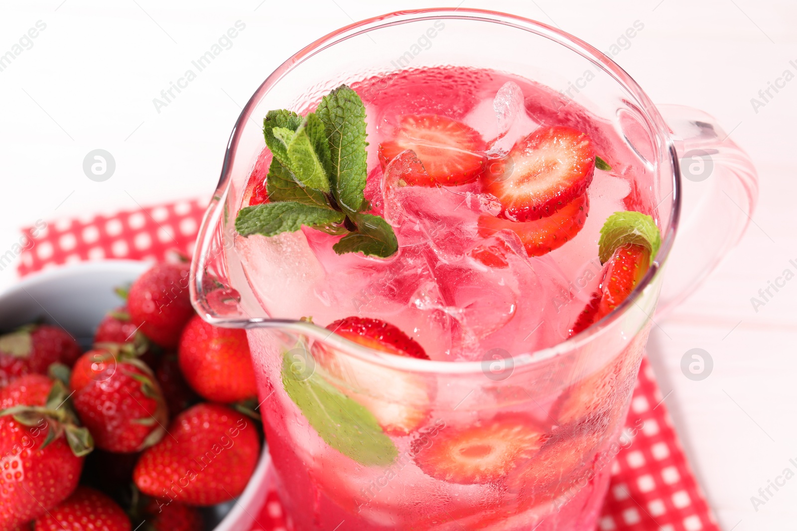 Photo of Freshly made strawberry lemonade with mint in jug on white wooden table, closeup