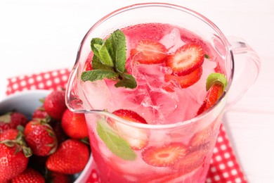 Photo of Freshly made strawberry lemonade with mint in jug on white wooden table, closeup