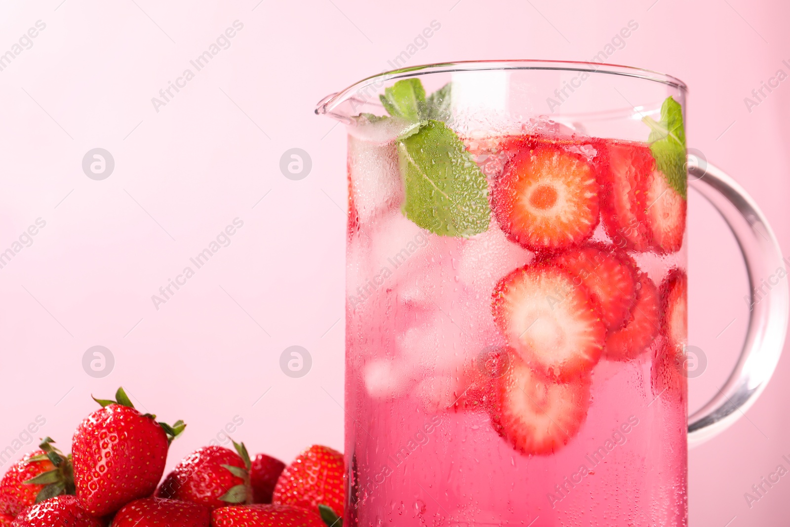 Photo of Freshly made strawberry lemonade with mint in jug on pink background, closeup. Space for text