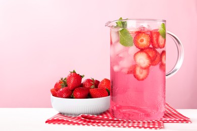 Photo of Freshly made strawberry lemonade with mint in jug on white wooden table against pink background, space for text