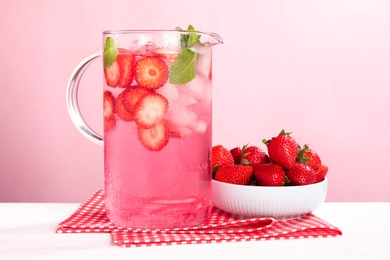 Photo of Freshly made strawberry lemonade with mint in jug on white wooden table against pink background