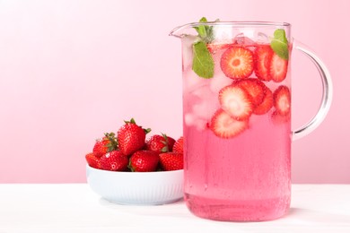 Photo of Freshly made strawberry lemonade with mint in jug on white wooden table against pink background