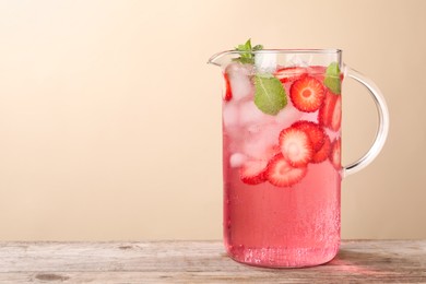 Photo of Freshly made strawberry lemonade with mint in jug on wooden table against beige background, space for text