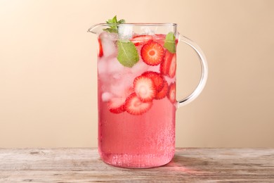 Photo of Freshly made strawberry lemonade with mint in jug on wooden table against beige background, space for text