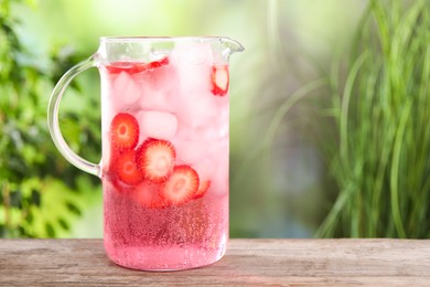 Freshly made strawberry lemonade in jug on wooden table outdoors, space for text