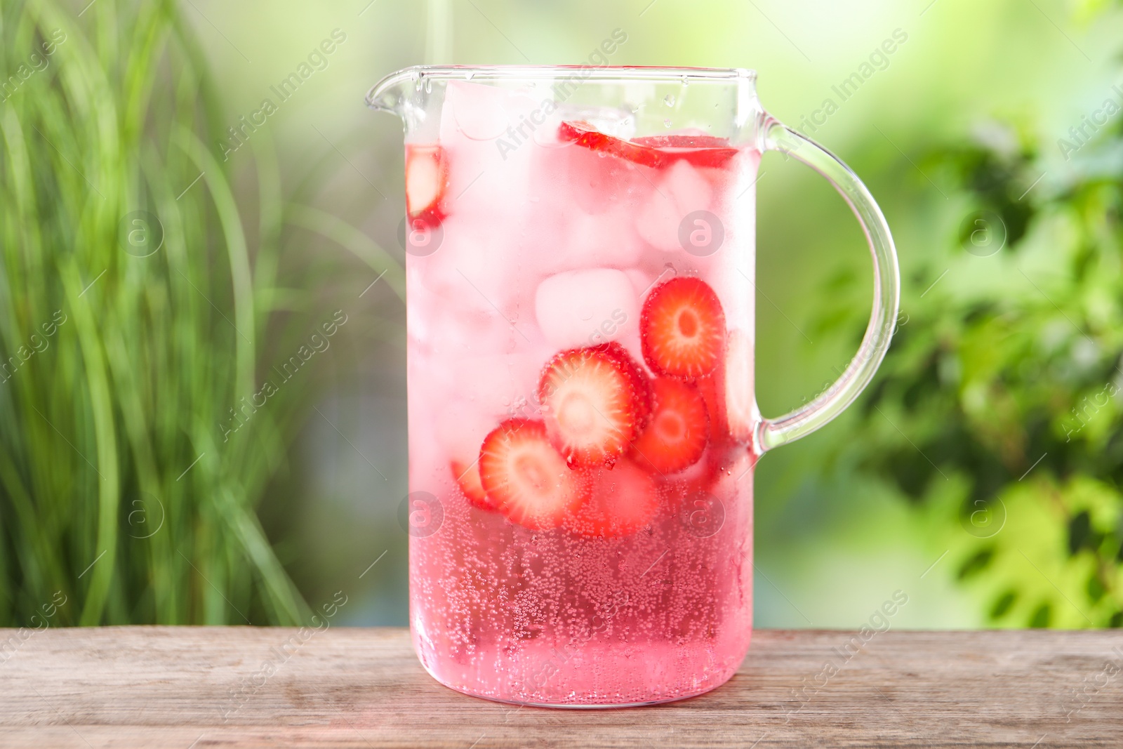 Photo of Freshly made strawberry lemonade in jug on wooden table outdoors