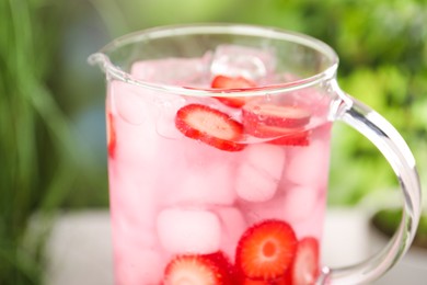 Photo of Freshly made strawberry lemonade in jug outdoors, closeup