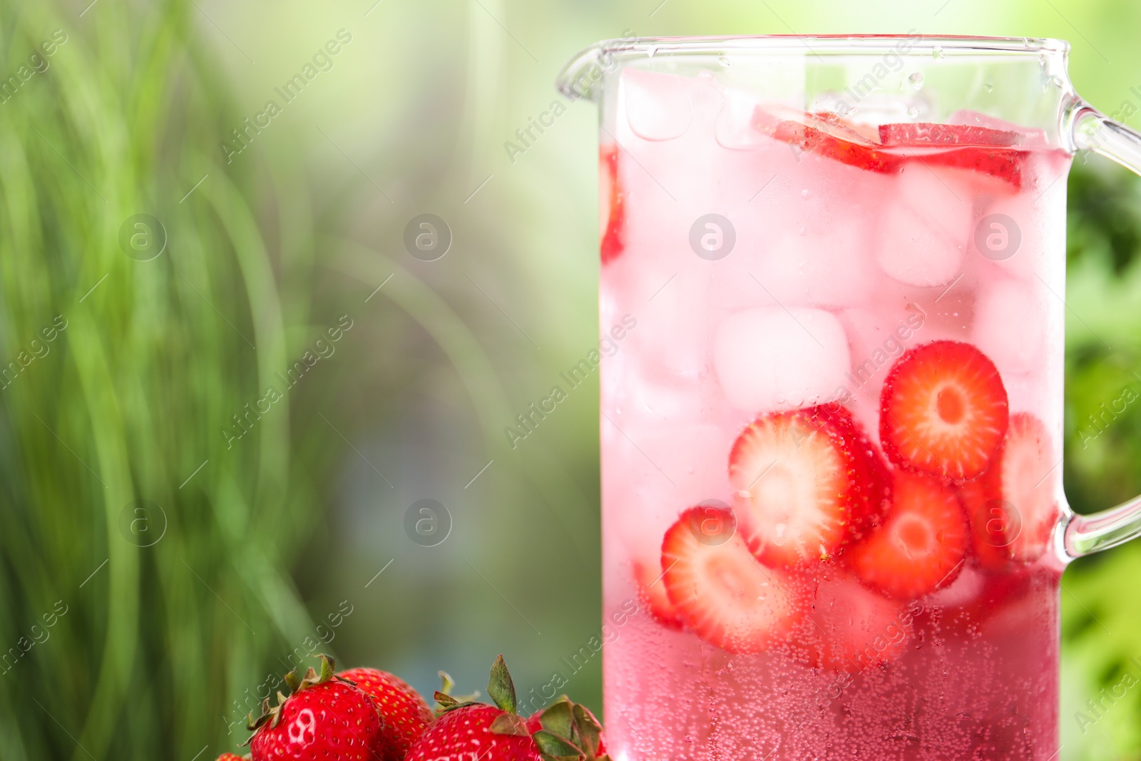 Photo of Freshly made strawberry lemonade in jug outdoors, closeup. Space for text