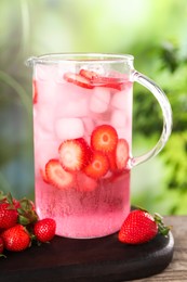 Photo of Freshly made strawberry lemonade in jug on wooden table outdoors