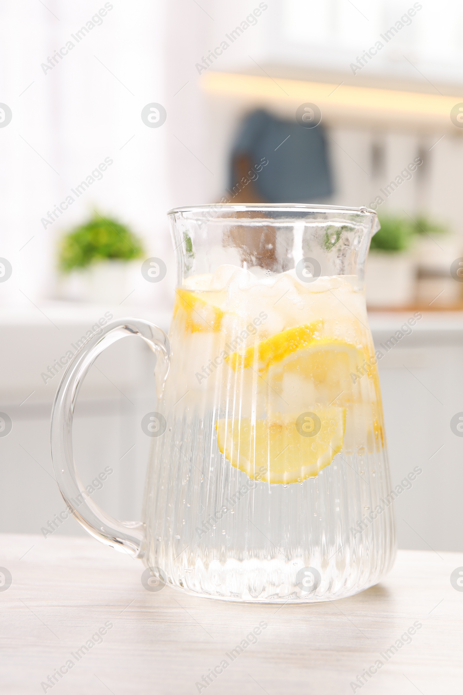 Photo of Freshly made lemonade in jug on white wooden table indoors