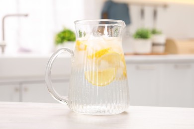 Photo of Freshly made lemonade in jug on white wooden table indoors