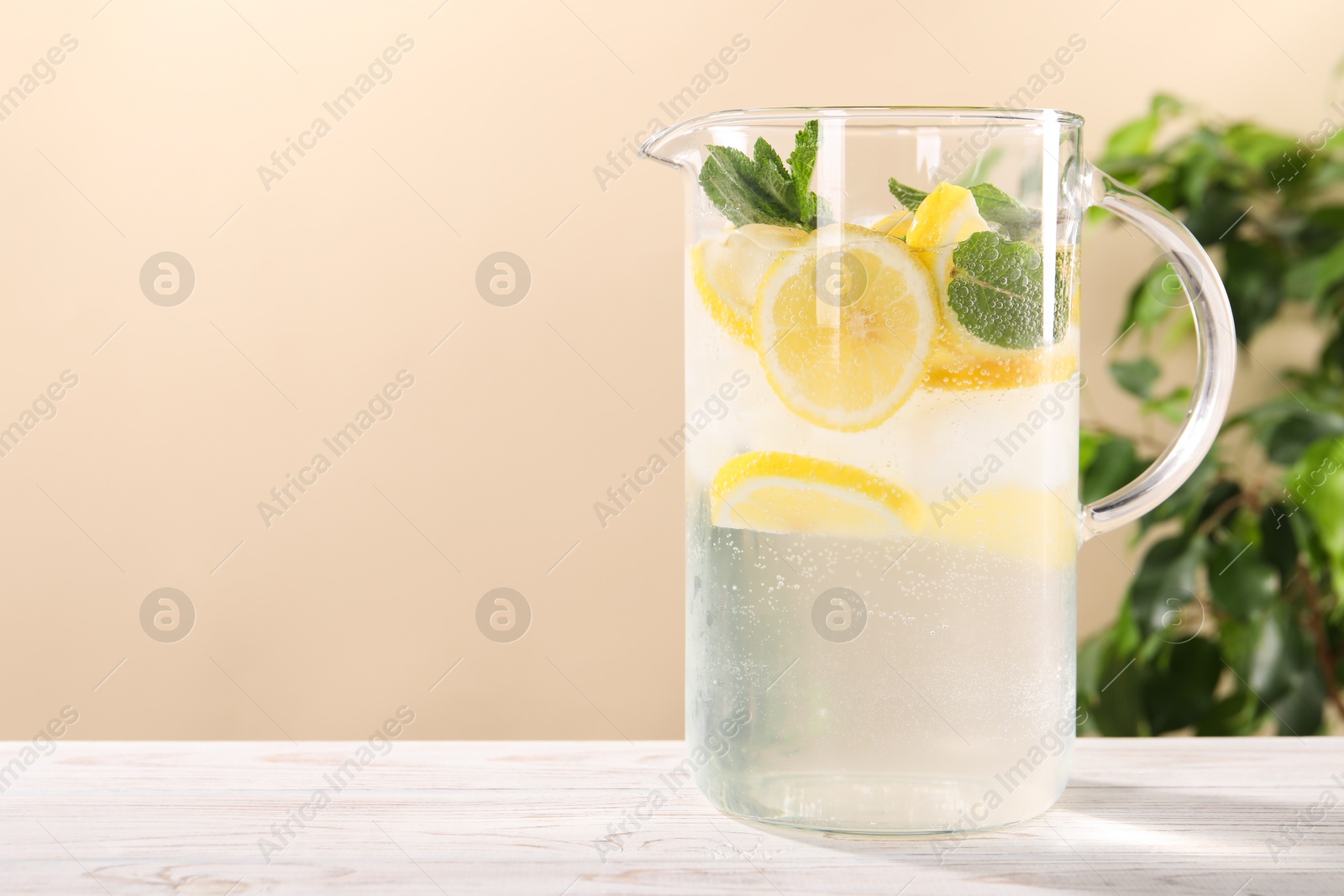 Photo of Freshly made lemonade with mint in jug on white wooden table against beige background, space for text