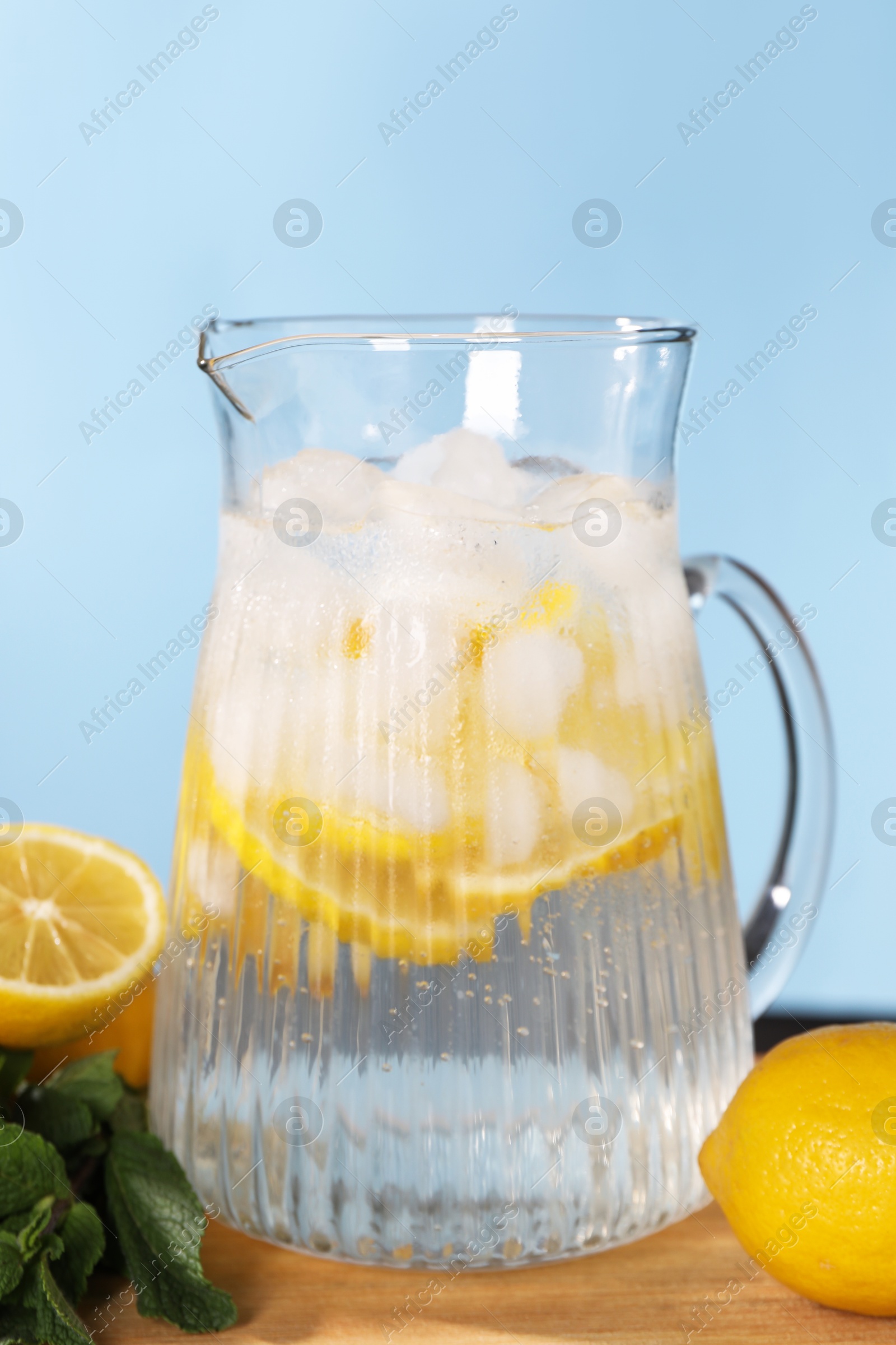 Photo of Freshly made lemonade with mint in jug on wooden table against light blue background