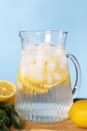 Photo of Freshly made lemonade with mint in jug on wooden table against light blue background