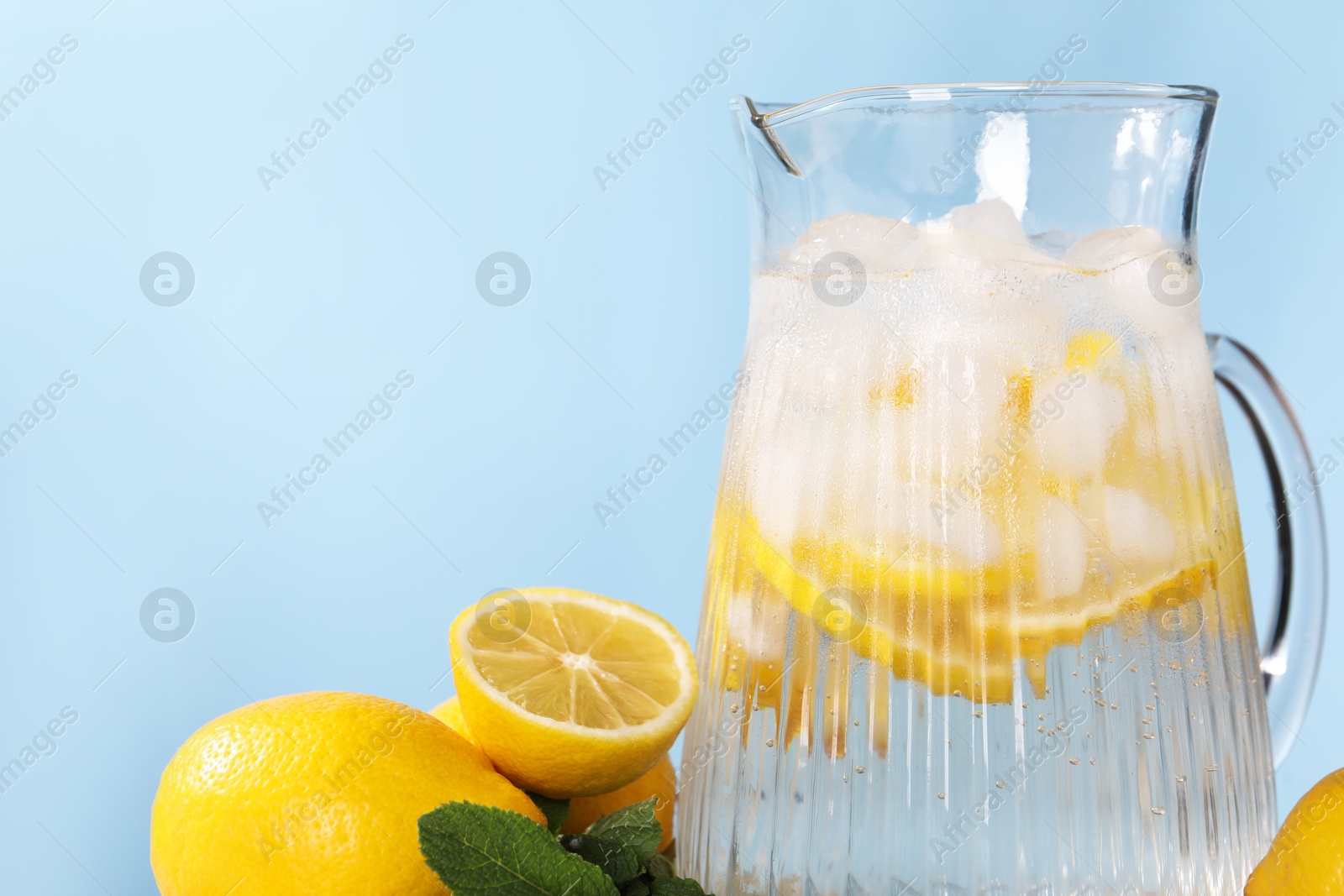 Photo of Freshly made lemonade with mint in jug on light blue background, closeup. Space for text