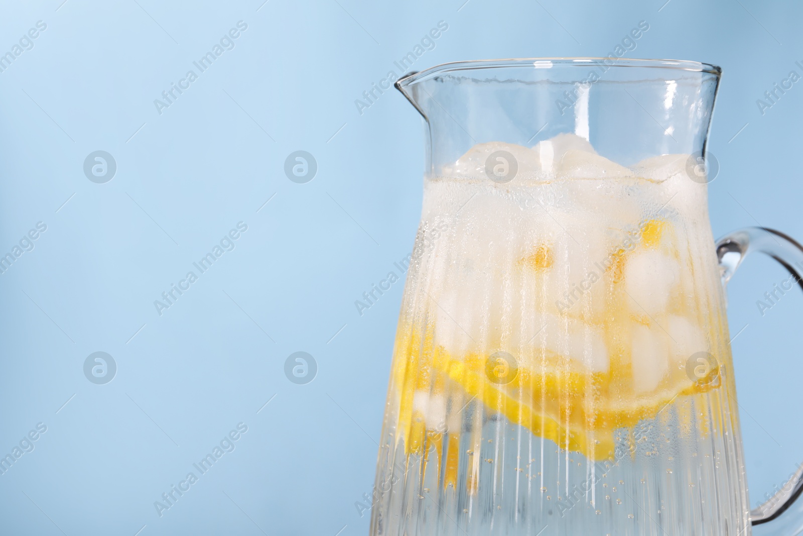 Photo of Freshly made lemonade in jug on light blue background, closeup. Space for text