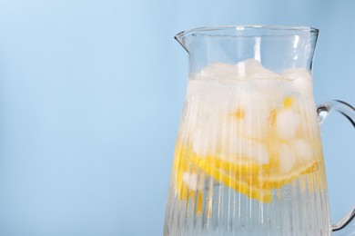 Photo of Freshly made lemonade in jug on light blue background, closeup. Space for text