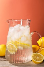 Photo of Freshly made lemonade in jug on wooden table against orange background