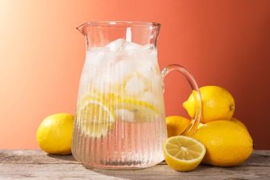 Photo of Freshly made lemonade in jug on wooden table against orange background