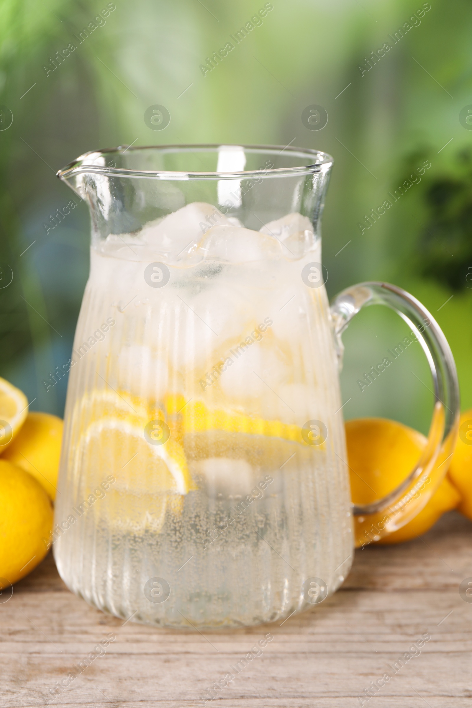 Photo of Freshly made lemonade in jug on wooden table outdoors