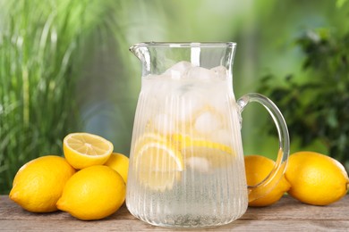 Photo of Freshly made lemonade in jug on wooden table outdoors