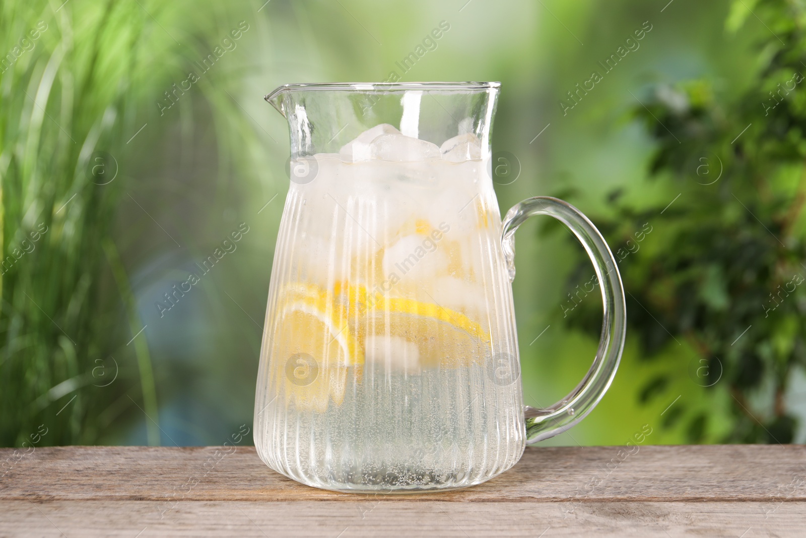 Photo of Freshly made lemonade in jug on wooden table outdoors