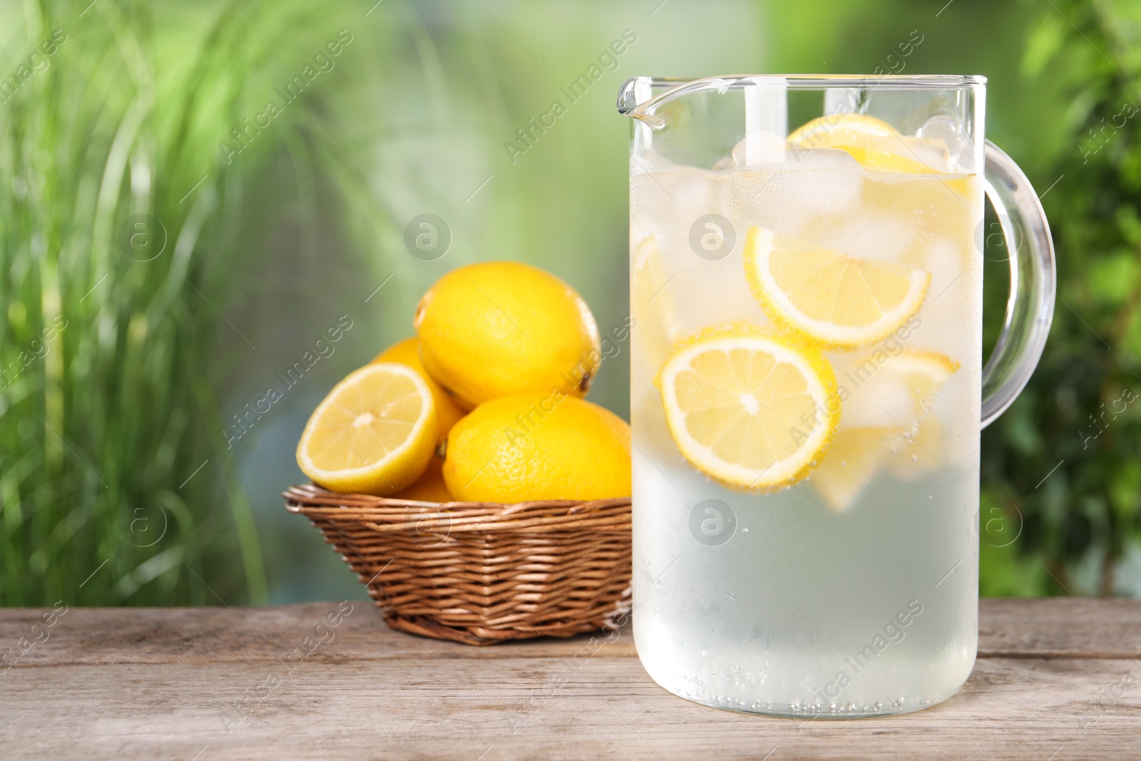 Photo of Freshly made lemonade in jug on wooden table outdoors