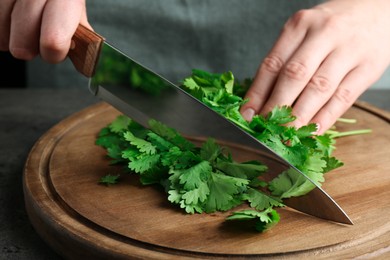 Photo of Woman cutting fresh coriander at table, closeup