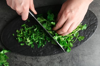 Woman cutting fresh coriander at grey textured table, top view