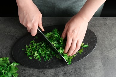 Woman cutting fresh coriander at grey textured table, top view