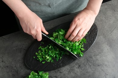 Woman cutting fresh coriander at grey textured table, top view