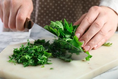 Woman cutting fresh coriander at white marble table, closeup