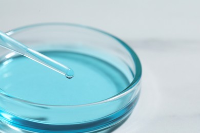 Photo of Dripping liquid from pipette into petri dish at white table, closeup