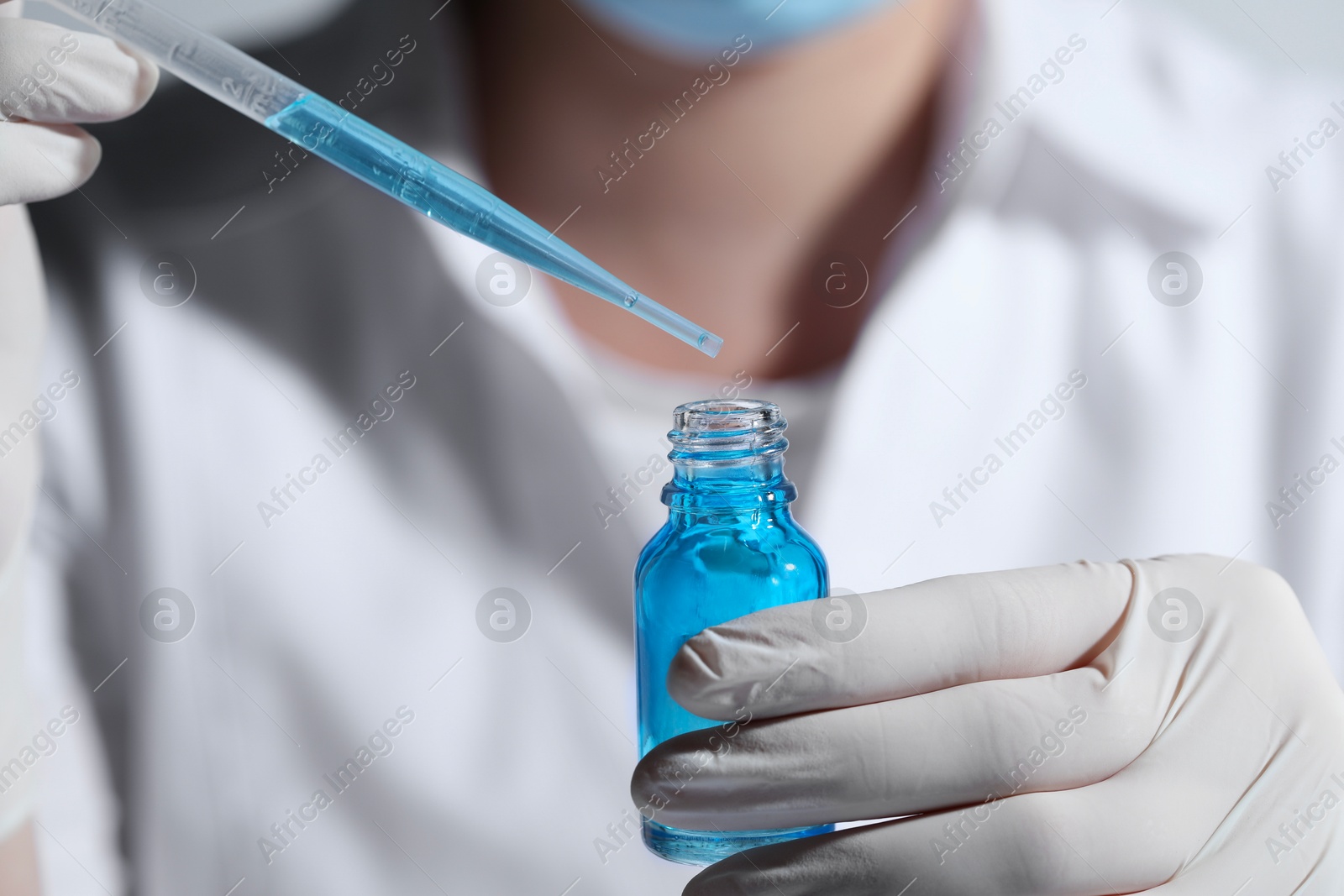 Photo of Scientist dripping liquid from pipette into glass bottle, closeup